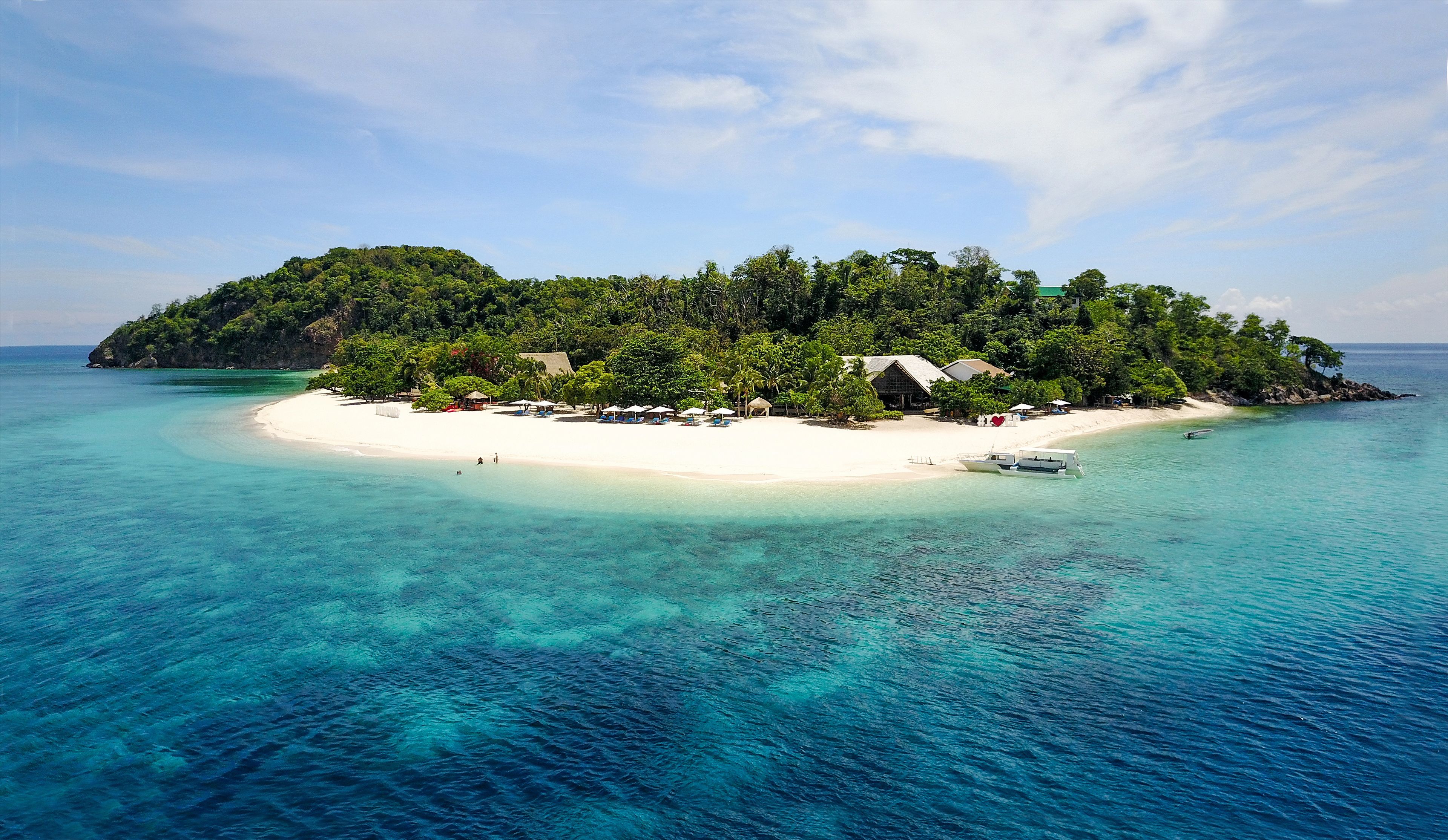 A tropical island with a white sandy beach, clear turquoise waters, and lush green vegetation.