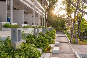 A modern building with a series of balconies and a pathway lined with greenery.