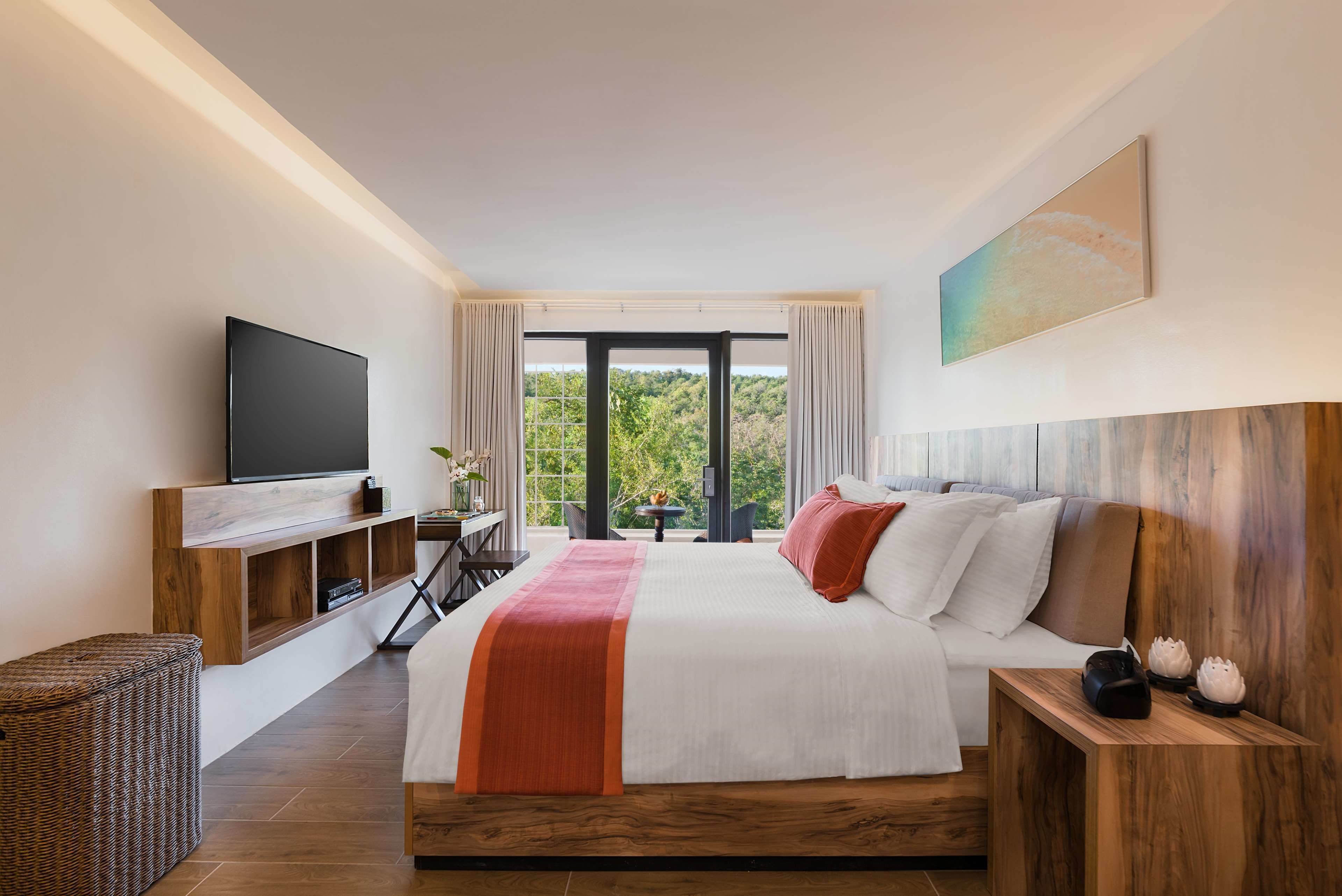 A modern hotel room with a large bed, a flat-screen TV, a wooden headboard, and a view of greenery through the window.