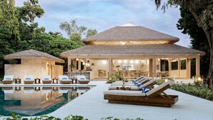 Un resort con piscina, sillas de descanso y un área de comedor techada.