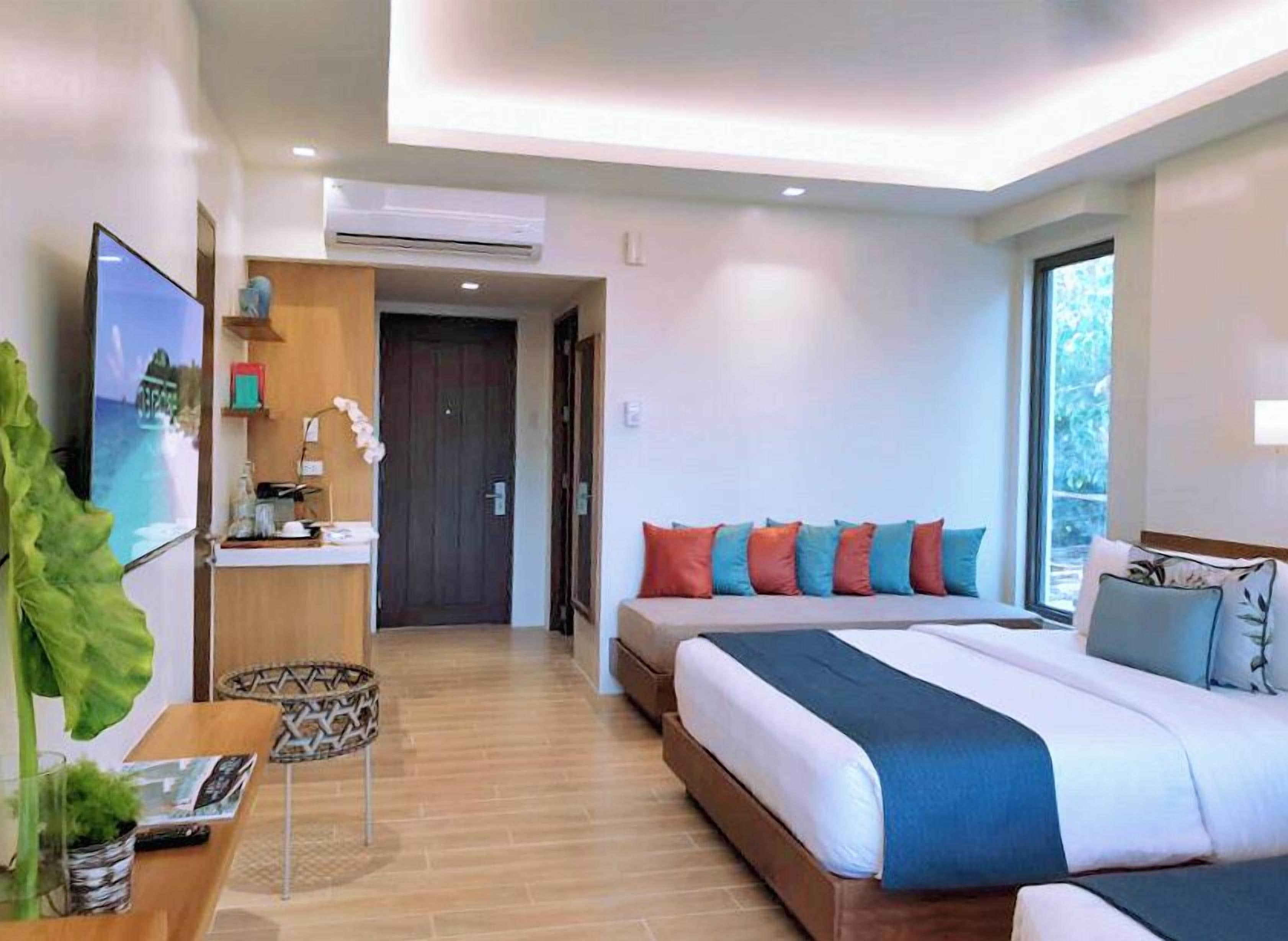 Una habitación de hotel moderna con una cama grande, un escritorio con una computadora y vistas al exterior.