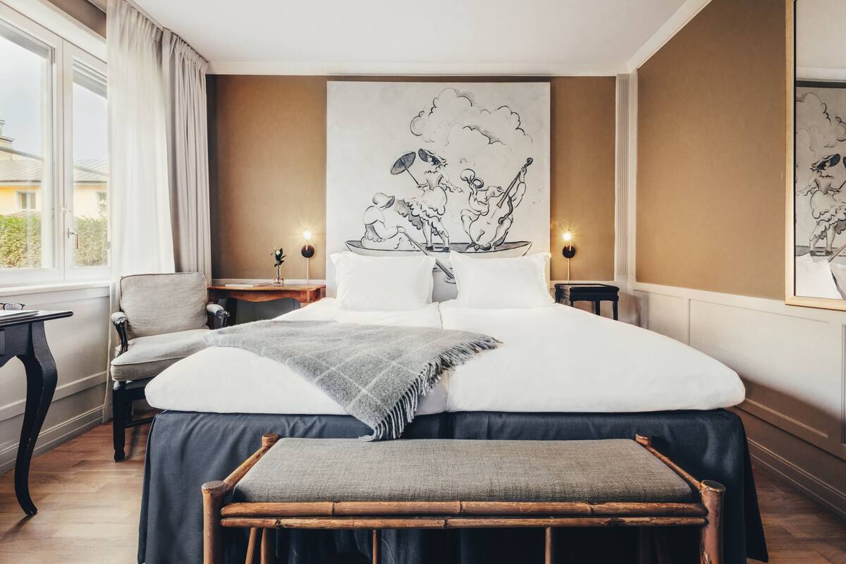 Una habitación de hotel con una cama grande, una silla, una mesita de noche y un buró.
