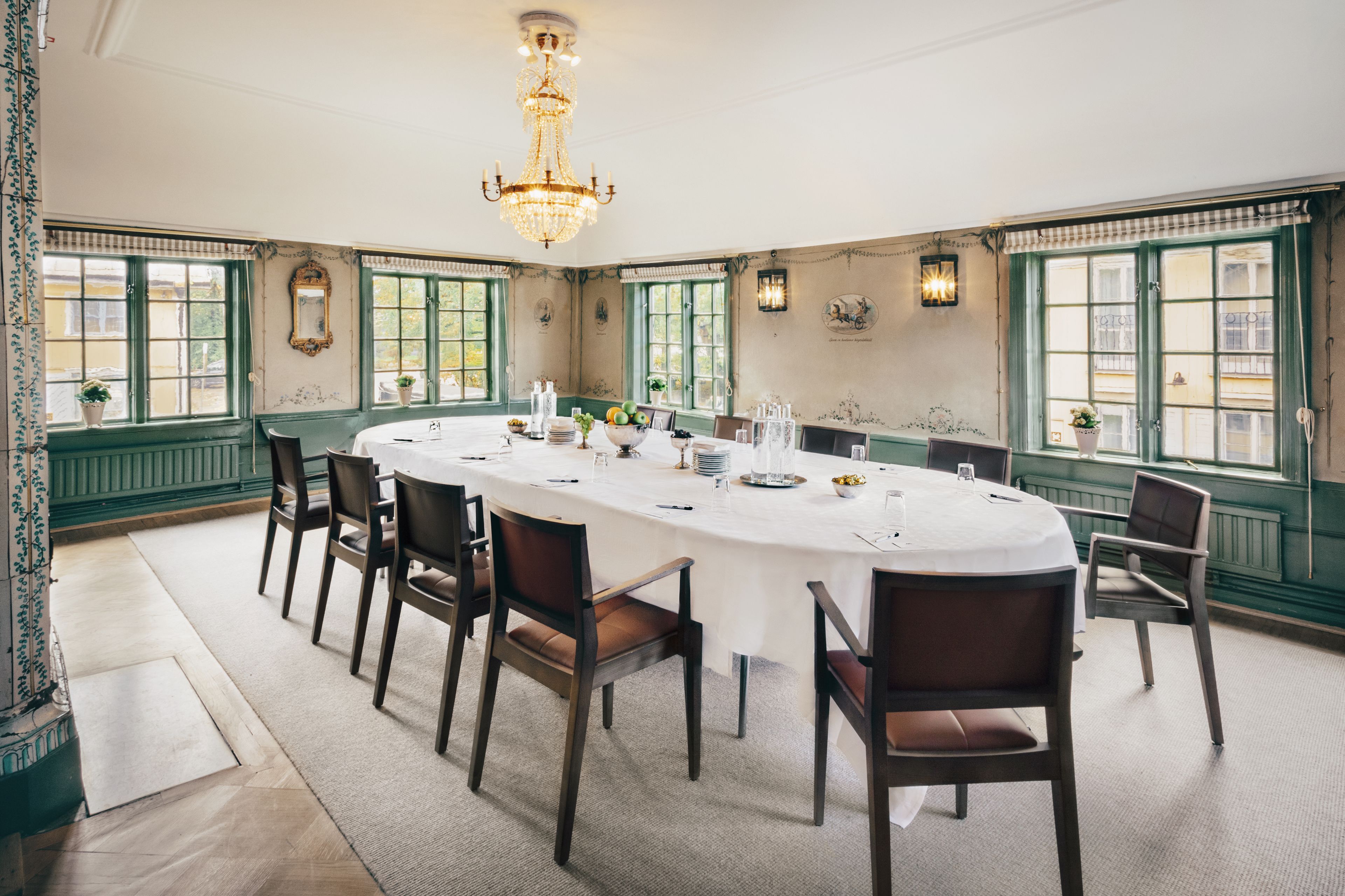 Un comedor formal con una amplia mesa ovalada, numerosas sillas, un candelabro y paredes revestidas de paneles verdes.