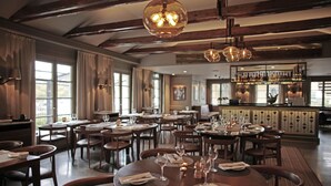 Un restaurante espacioso con numerosas mesas, vigas de madera en el techo y una zona de bar al fondo.