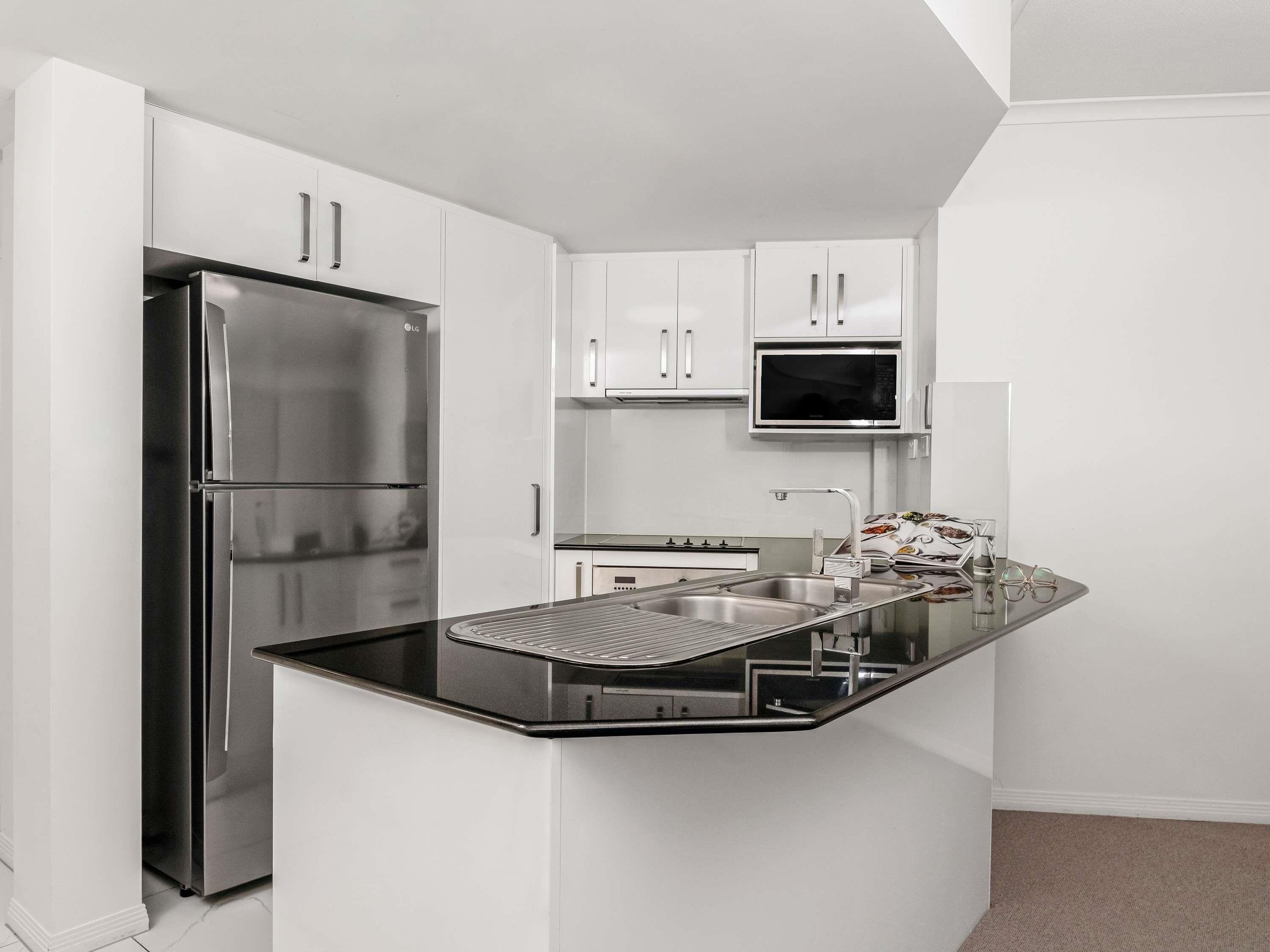 Una cocina moderna con armarios blancos, un refrigerador de acero inoxidable, un microondas y un fregadero con encimera de acero inoxidable.