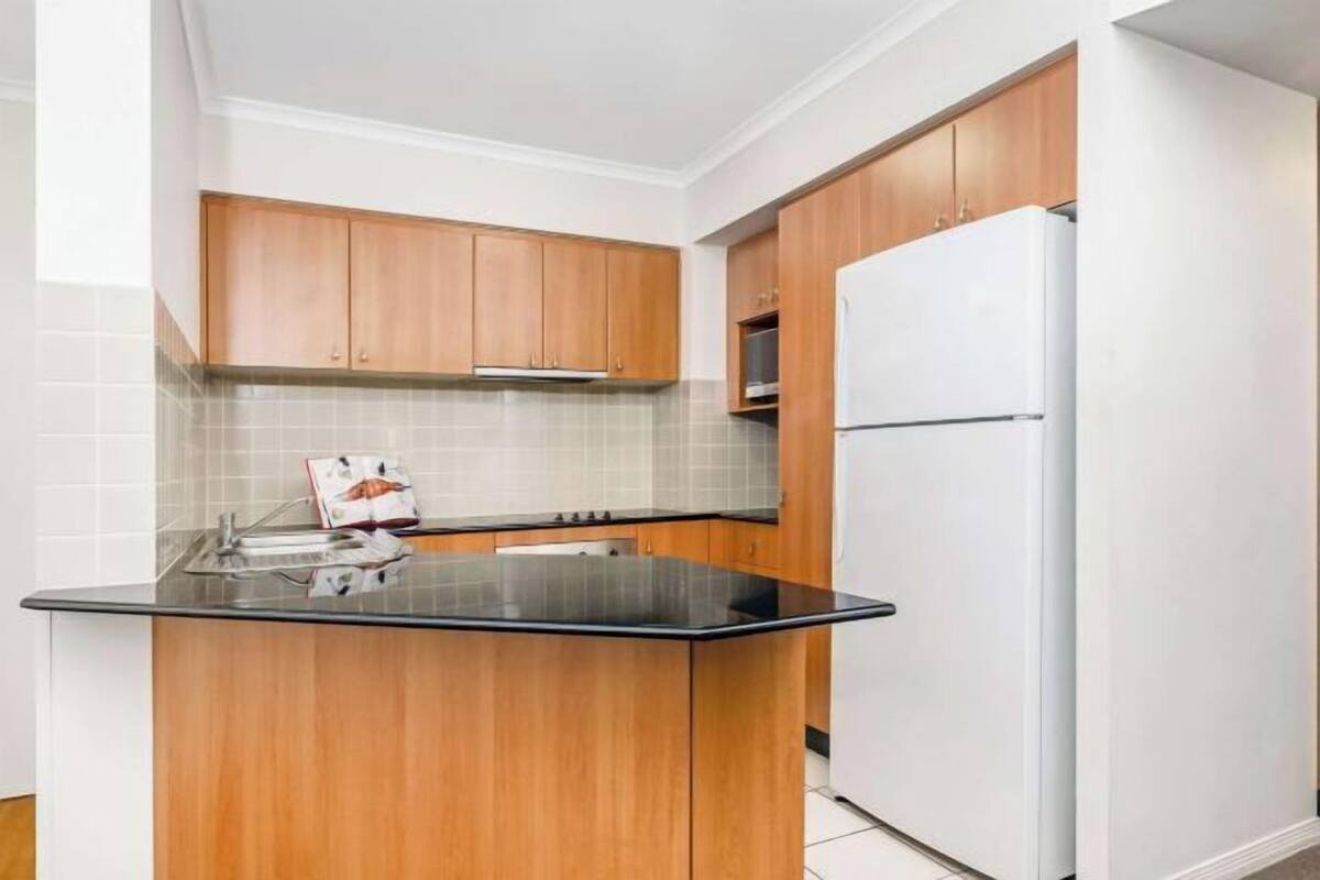 A kitchen with wooden cabinets, a black countertop, and a white refrigerator.
