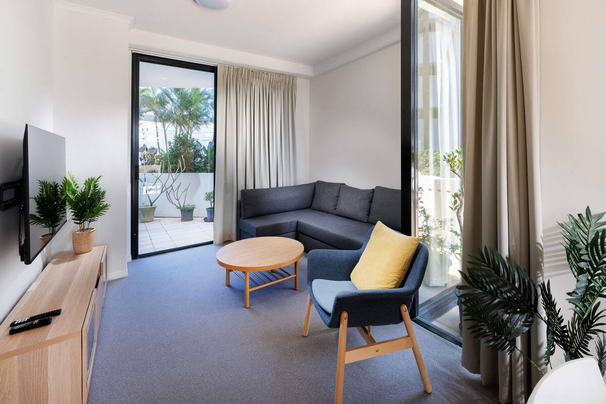 A modern living room with a sofa, a chair, a coffee table, a TV, and potted plants.