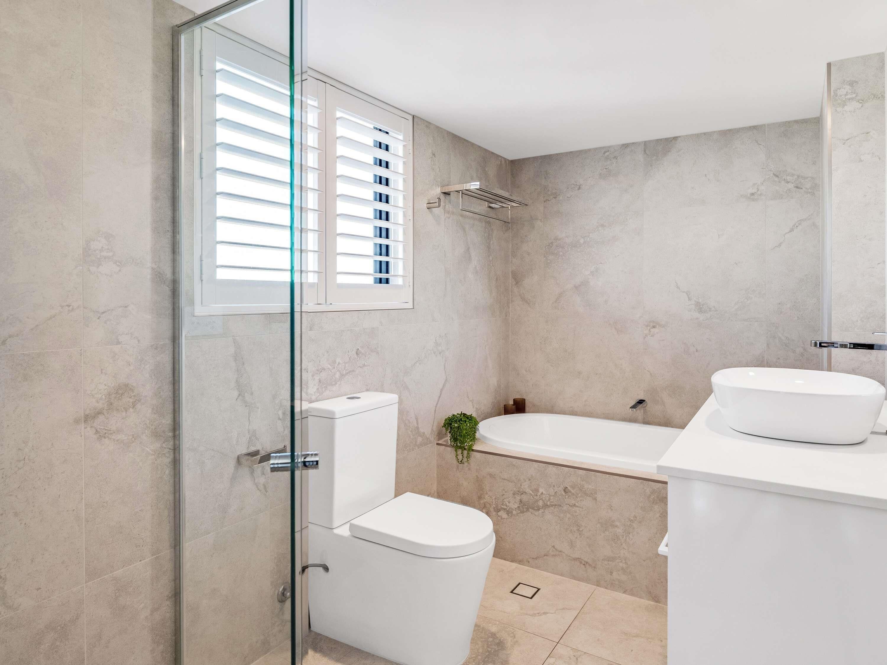 A modern bathroom with a glass shower enclosure, a toilet, a bathtub, and a white sink.