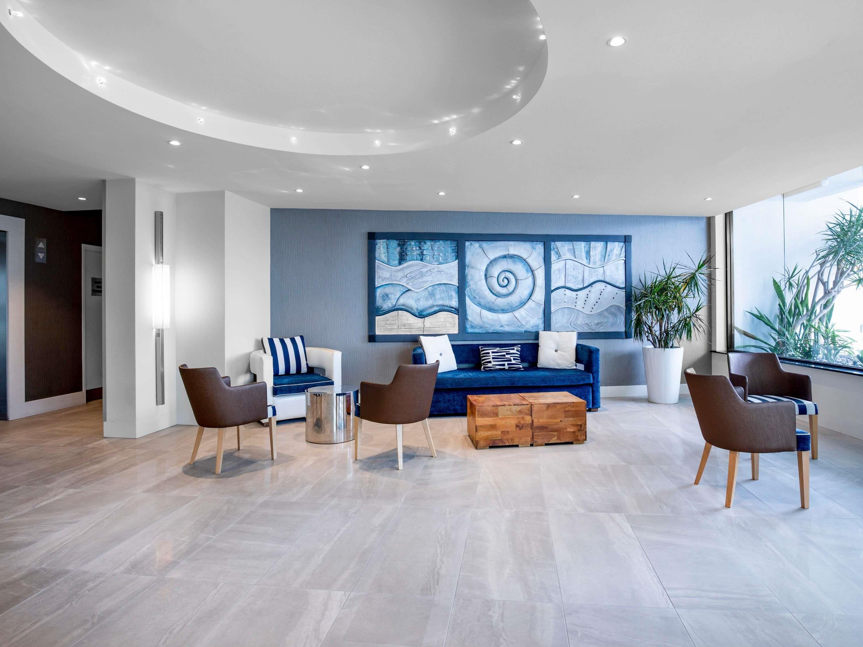 Una sala de estar moderna con un sofá azul, sillas marrones, una mesa de centro de madera y arte abstracto en la pared.