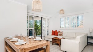 A modern living room with a wooden dining table set for four, a white sofa, and a wooden coffee table. - Mantra Coolangatta Beach (Coolangatta)