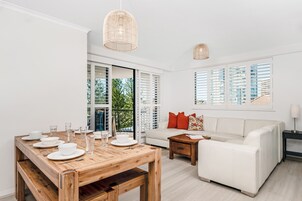 A modern living room with a wooden dining table set for four, a white sofa, and a wooden coffee table.