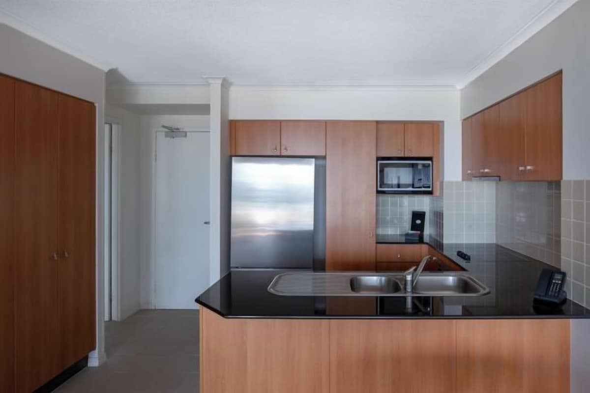 Cocina moderna con armarios de madera, refrigerador de acero inoxidable y encimera negra.