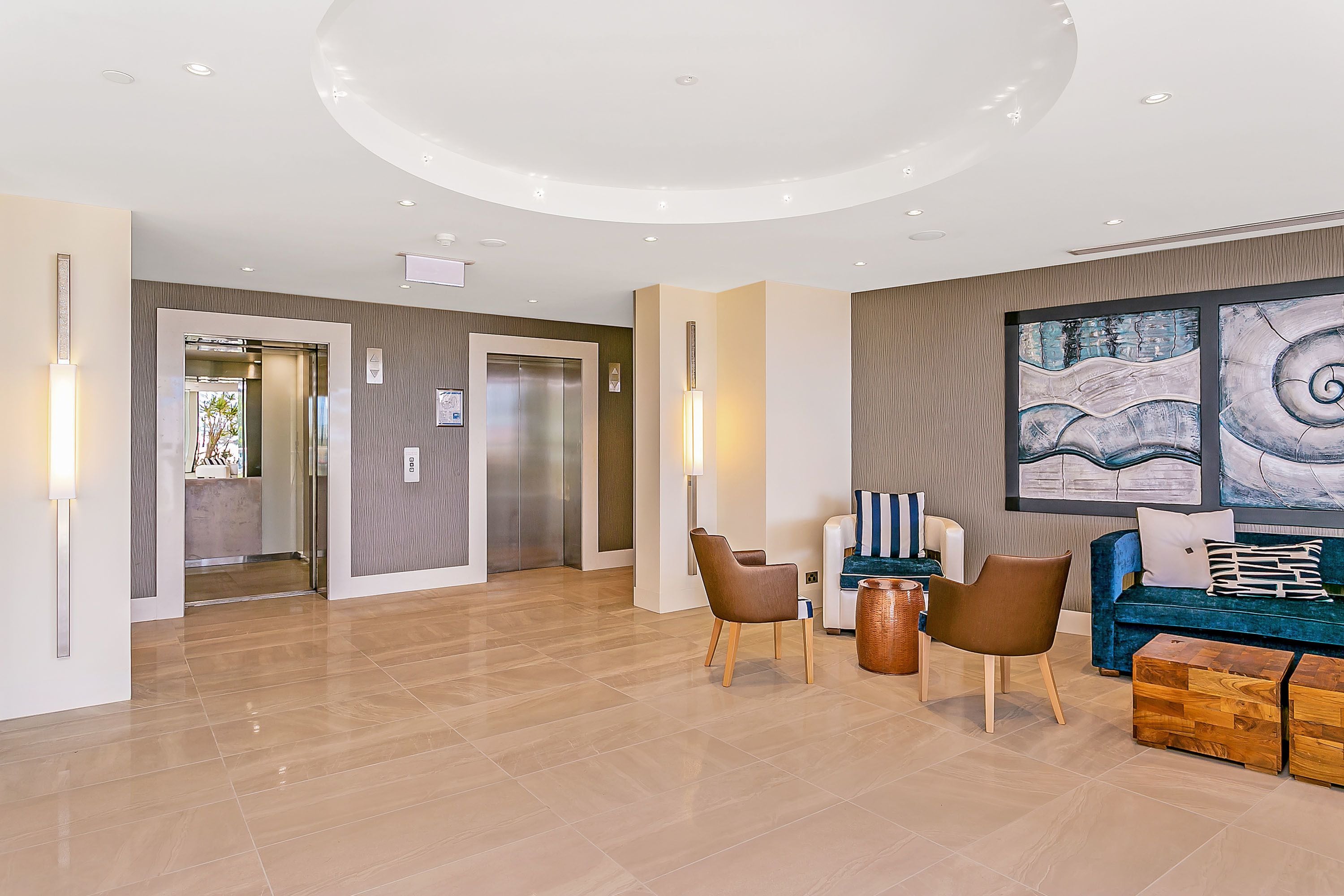 En rymlig lobby med modern design, med en sittgrupp bestående av en blå soffa och bruna fåtöljer, ett soffbord i trä och en stor, abstrakt målning på väggen.