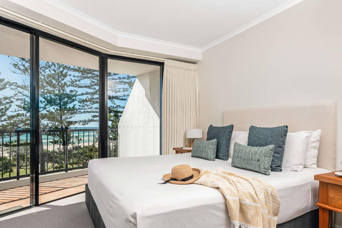 A hotel room with a bed, a balcony with a view, and a large window.