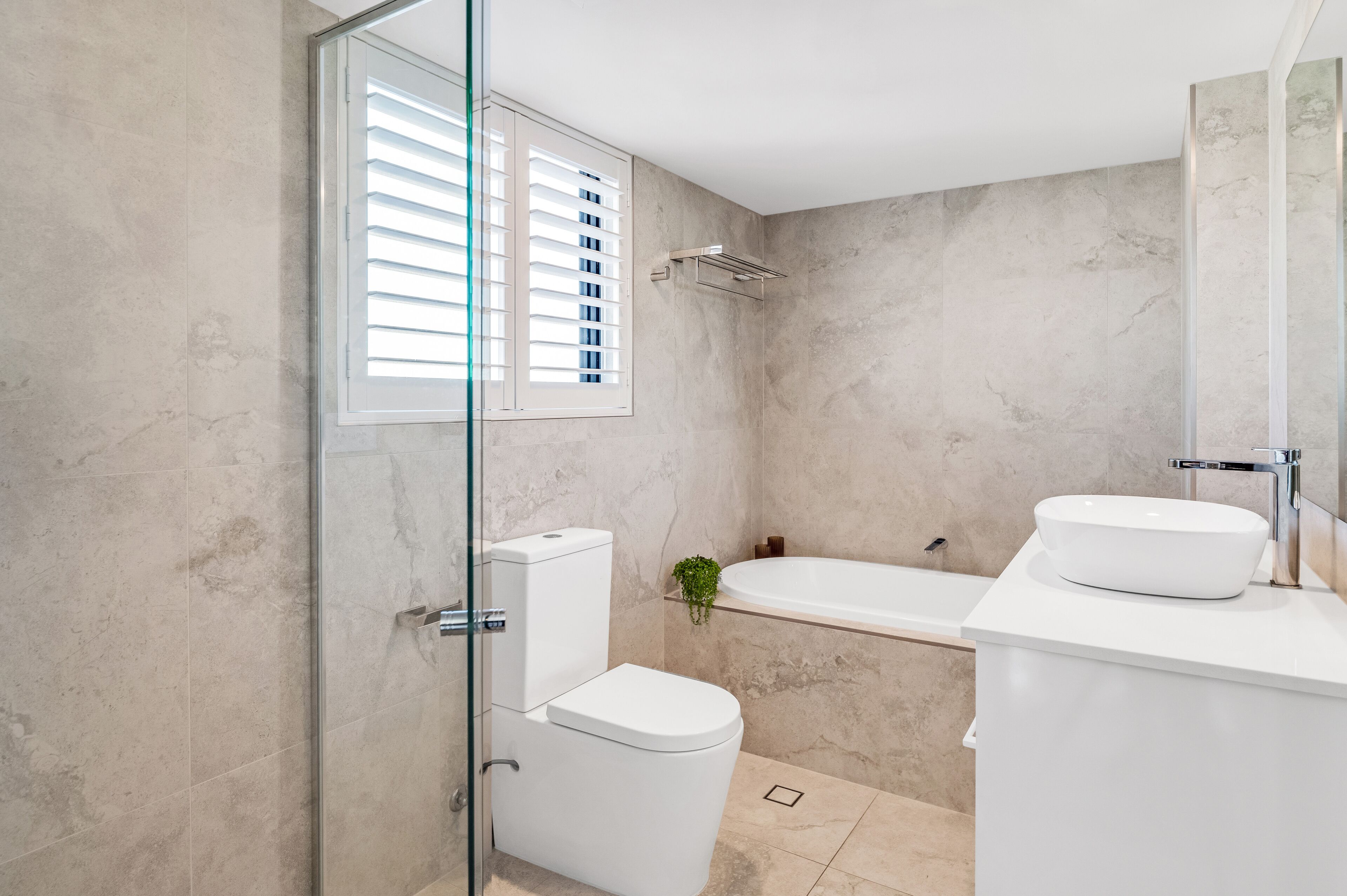 A modern bathroom with a glass shower enclosure, a white toilet, a bathtub, and a sink with a mirror.