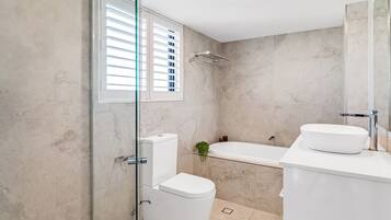 A modern bathroom with a glass shower enclosure, a white toilet, a bathtub, and a sink with a mirror.