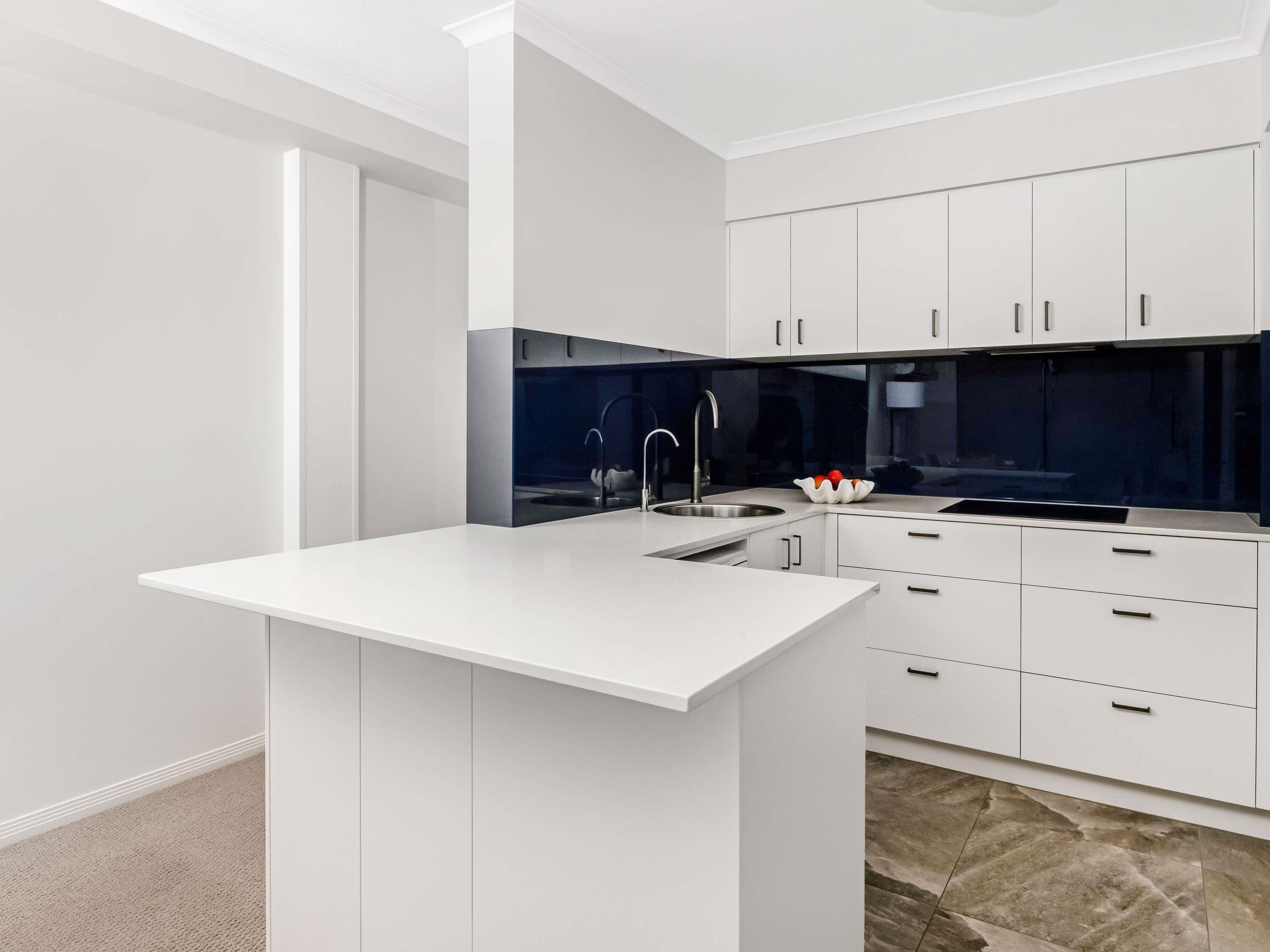 A modern kitchen with white cabinetry, a central island, and a dark backsplash.