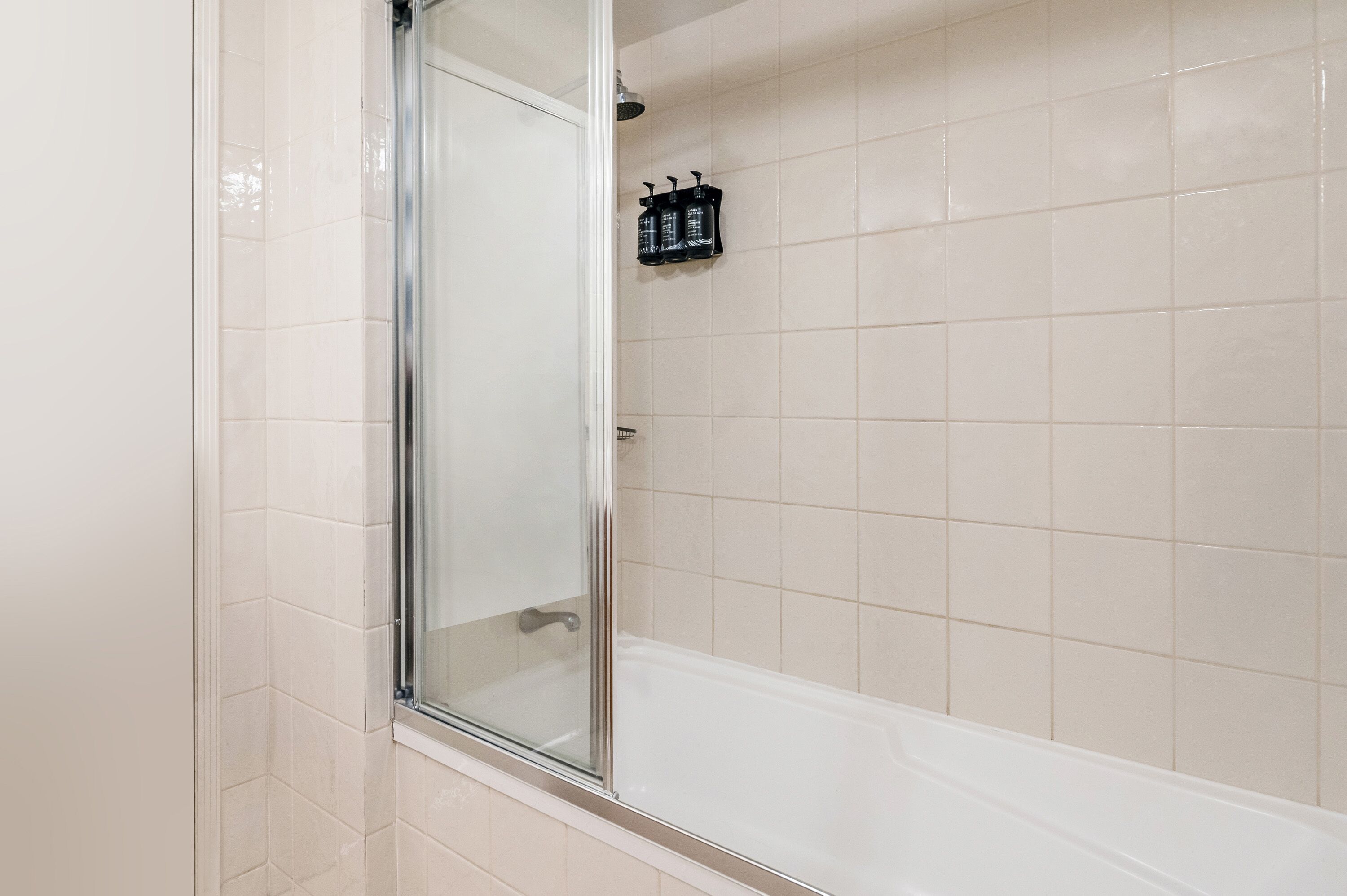 Een badkamer met een glazen douchecabine, een witte badkuip en een zeepdispenser aan de muur.