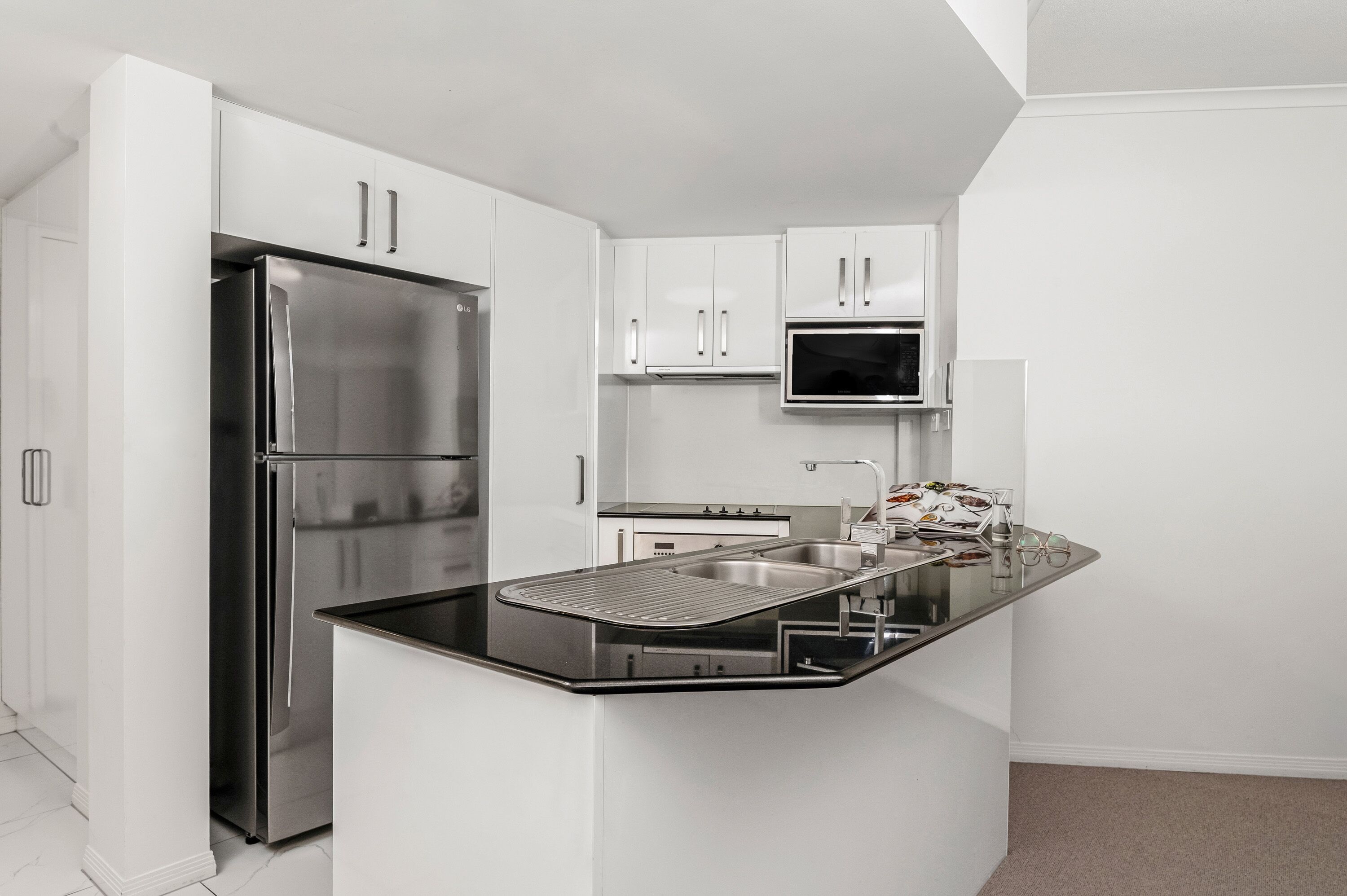 Una cocina moderna con armarios blancos, un refrigerador de acero inoxidable, un microondas y una isla de encimera negra con un fregadero.