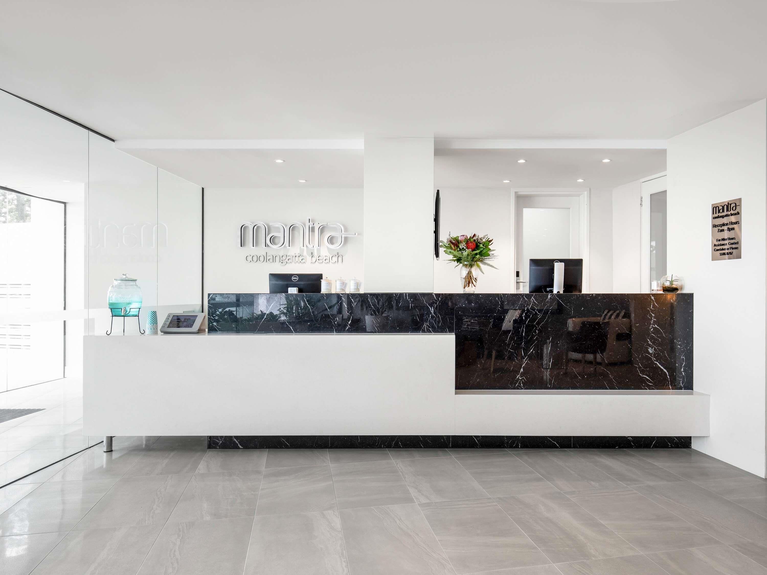 A modern reception desk with a marble top, a glass water dispenser, and a vase with flowers.