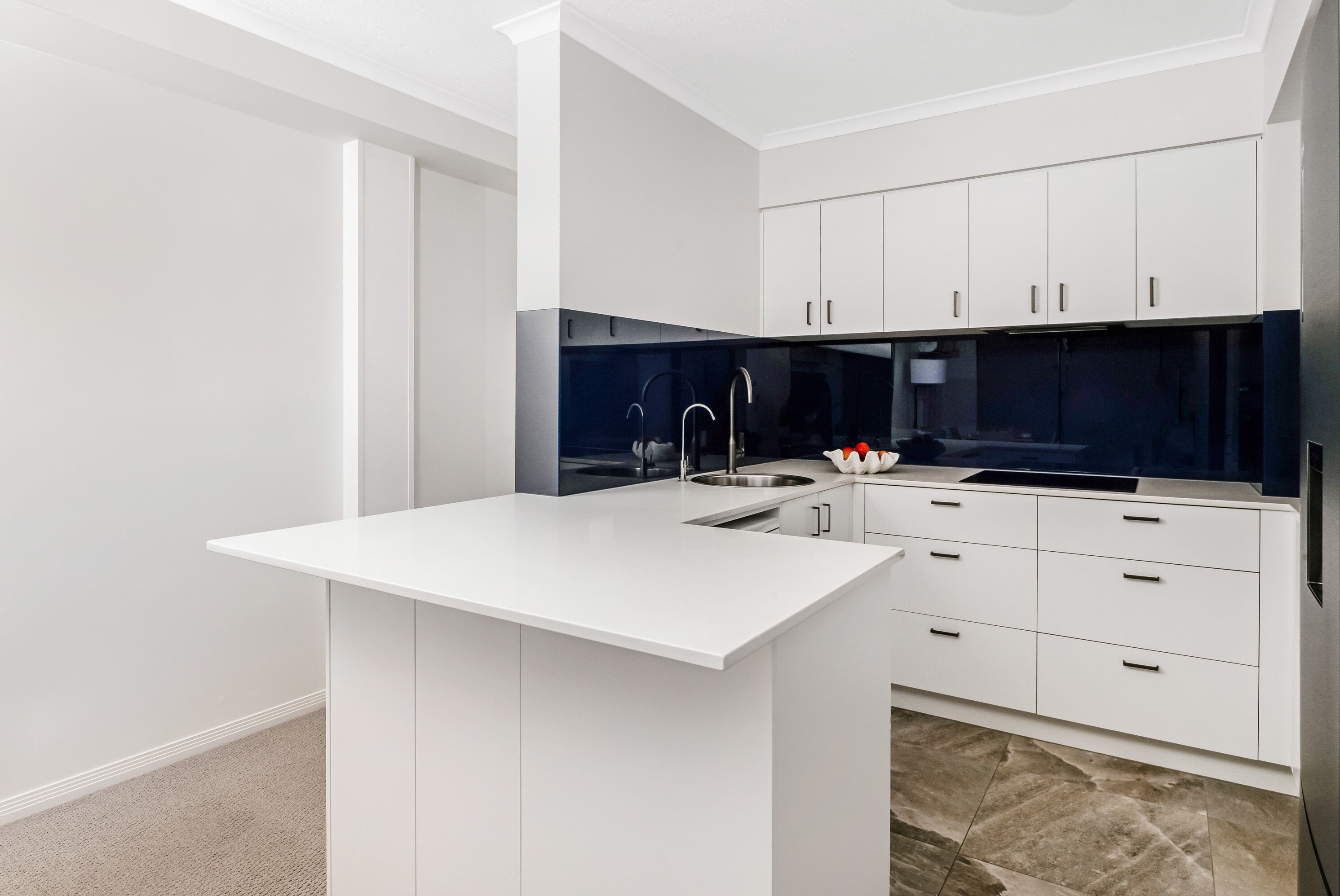 A modern kitchen with white cabinetry, a central island, and a dark backsplash.