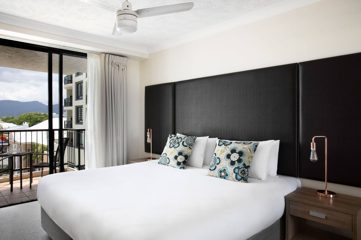 Ein Hotelzimmer mit einem großen Bett, einem Nachttisch, einem Schreibtisch und einem Balkon mit Bergblick.