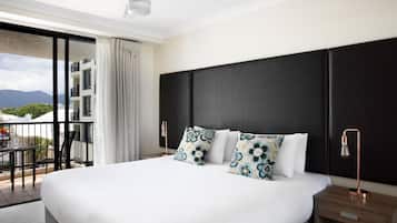 A hotel room with a large bed, a nightstand, a desk, and a balcony with a view of mountains.