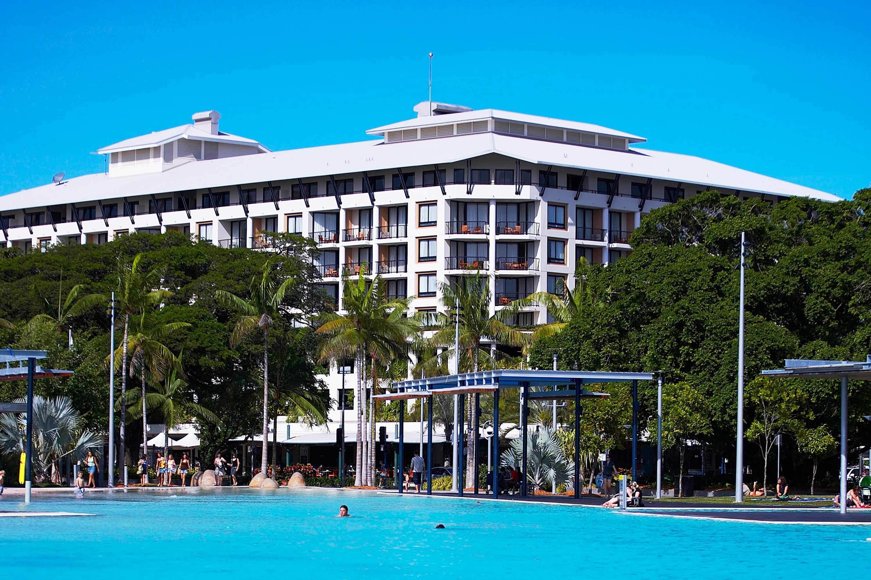 A hotel with a large swimming pool surrounded by palm trees and covered areas.