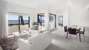 A modern living room with a white sofa, a glass coffee table, and a dining area with a table set for four. - Mantra Esplanade (Cairns)