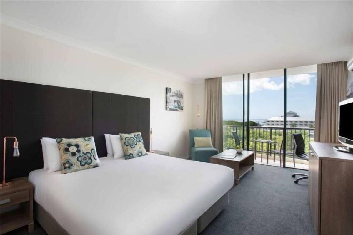 Ein Hotelzimmer mit einem großen Bett, einem Schreibtisch mit Fernseher, einem Sessel und einem Balkon mit Blick.