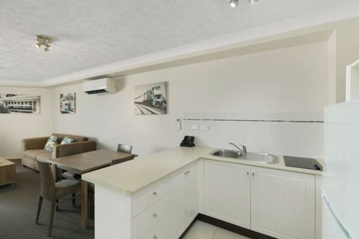 A compact kitchen with white cabinets, a dining area with a table and chairs, and a sofa.