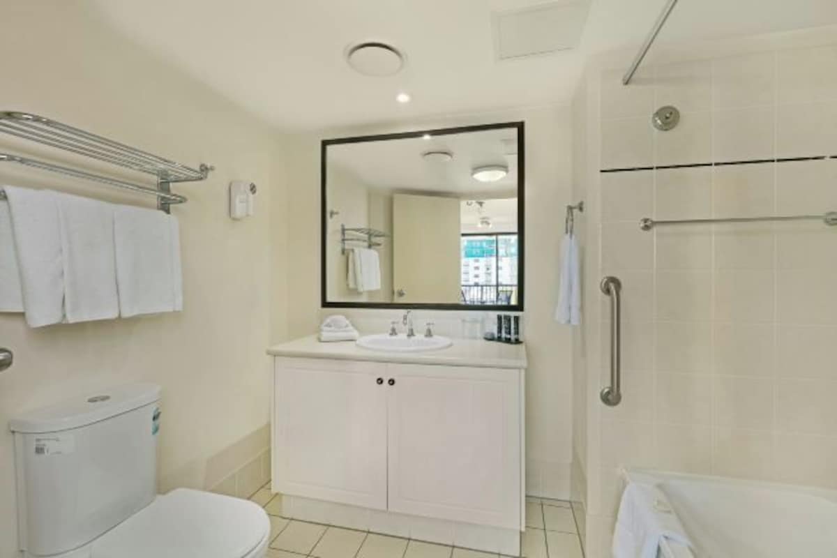 A bathroom with a toilet, sink, mirror, towel rack, and shower.