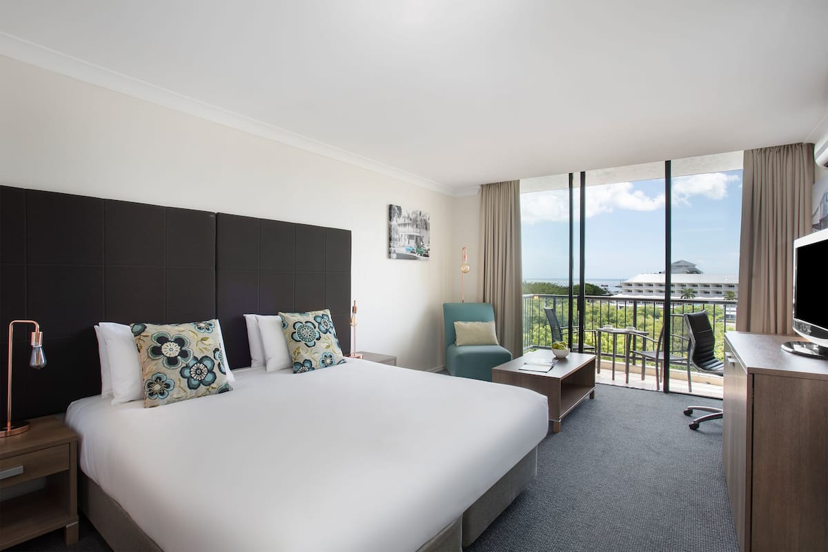 Ein Hotelzimmer mit einem großen Bett, einem Schreibtisch, einem Sessel und Blick auf die Stadt.