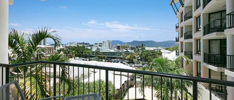 A balcony with a view of a cityscape, including a Woolworths store, palm trees, and distant mountains.