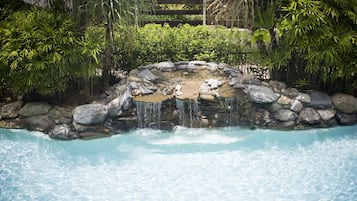 A natural pool with a waterfall surrounded by rocks and lush greenery.