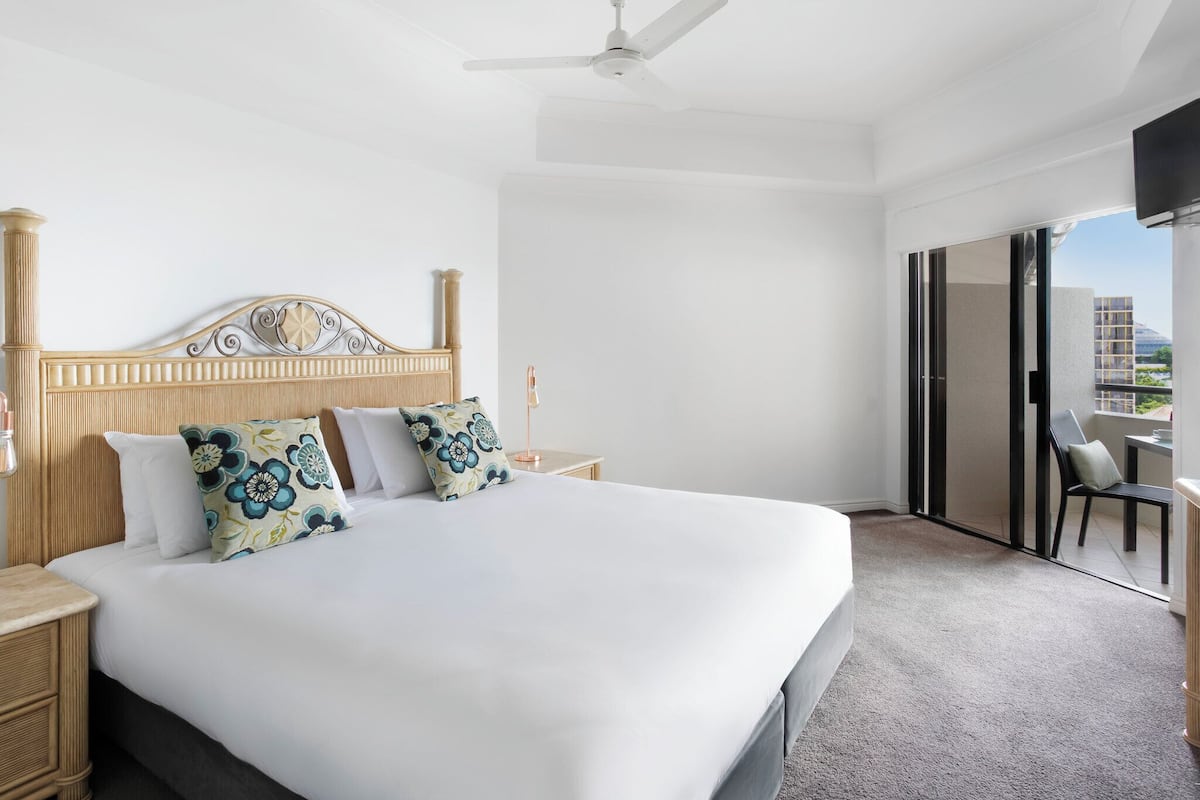 Ein Hotelzimmer mit einem großen Bett, einem Deckenventilator, einem Nachttisch und Blick durch eine Schiebetür nach außen.