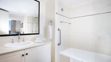 Casa de banho moderna com lavatório branco, espelho e banheira. Existem barras de apoio no chuveiro e um porta-toalhas.