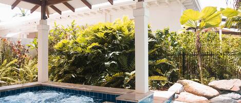 A hot tub area with a tiled edge, surrounded by lush greenery and rocks.