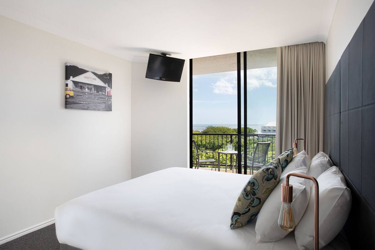 Ein Hotelzimmer mit einem großen Bett, einem Flachbildfernseher, einem Bild an der Wand und einem Balkon mit Blick.
