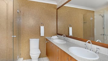 A modern bathroom with a glass shower enclosure, a toilet, a sink with a mirror, and a vanity with cabinets.