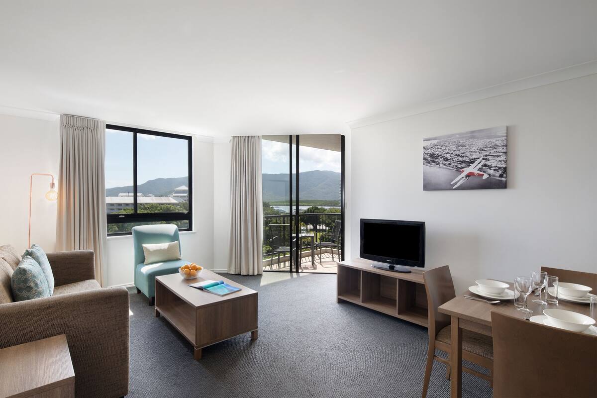 Ein modernes Hotelzimmer mit großem Fenster, Flachbildfernseher, Essbereich und einer Sitzecke.
