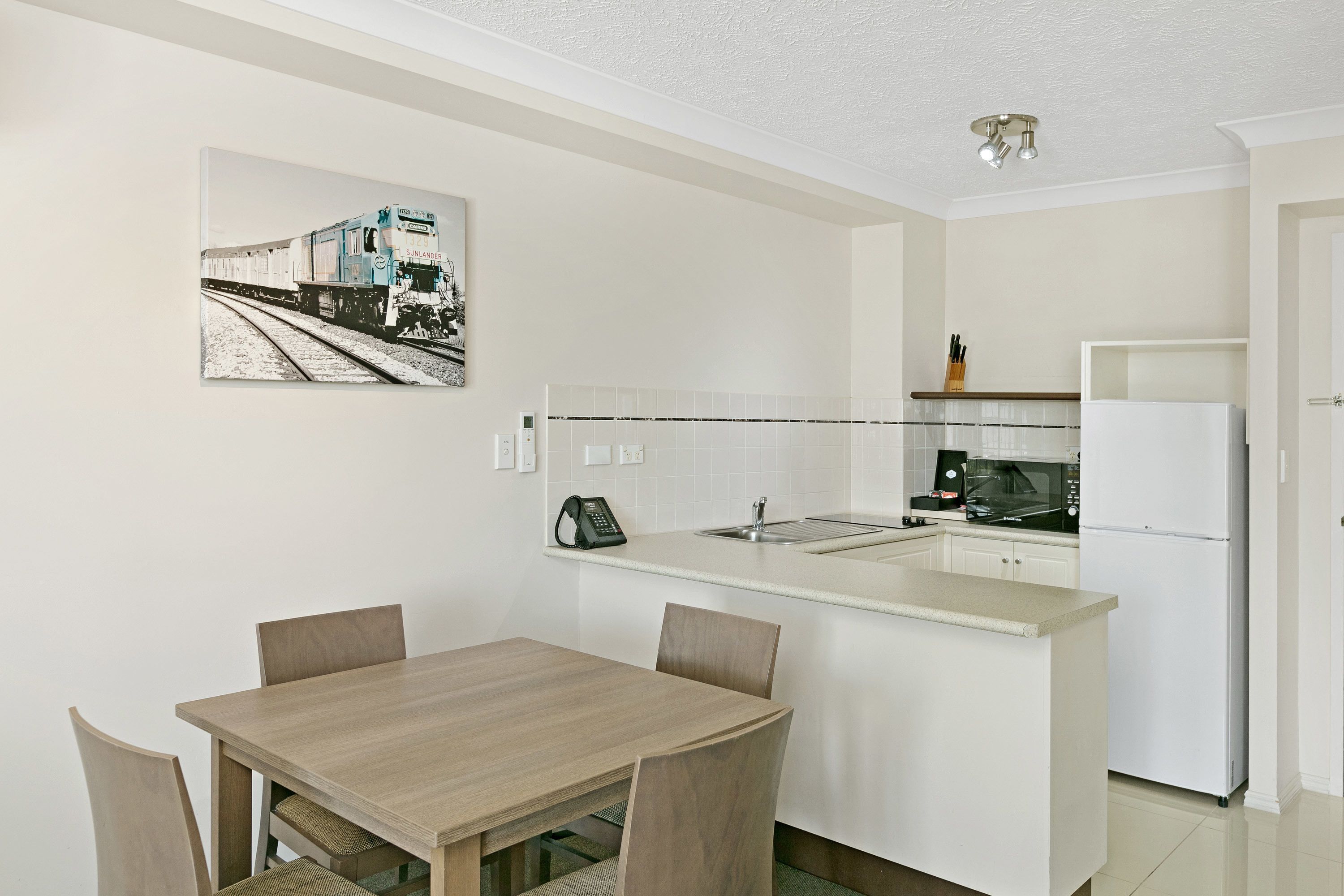 A compact kitchen with a dining area, featuring a microwave, refrigerator, and a telephone.