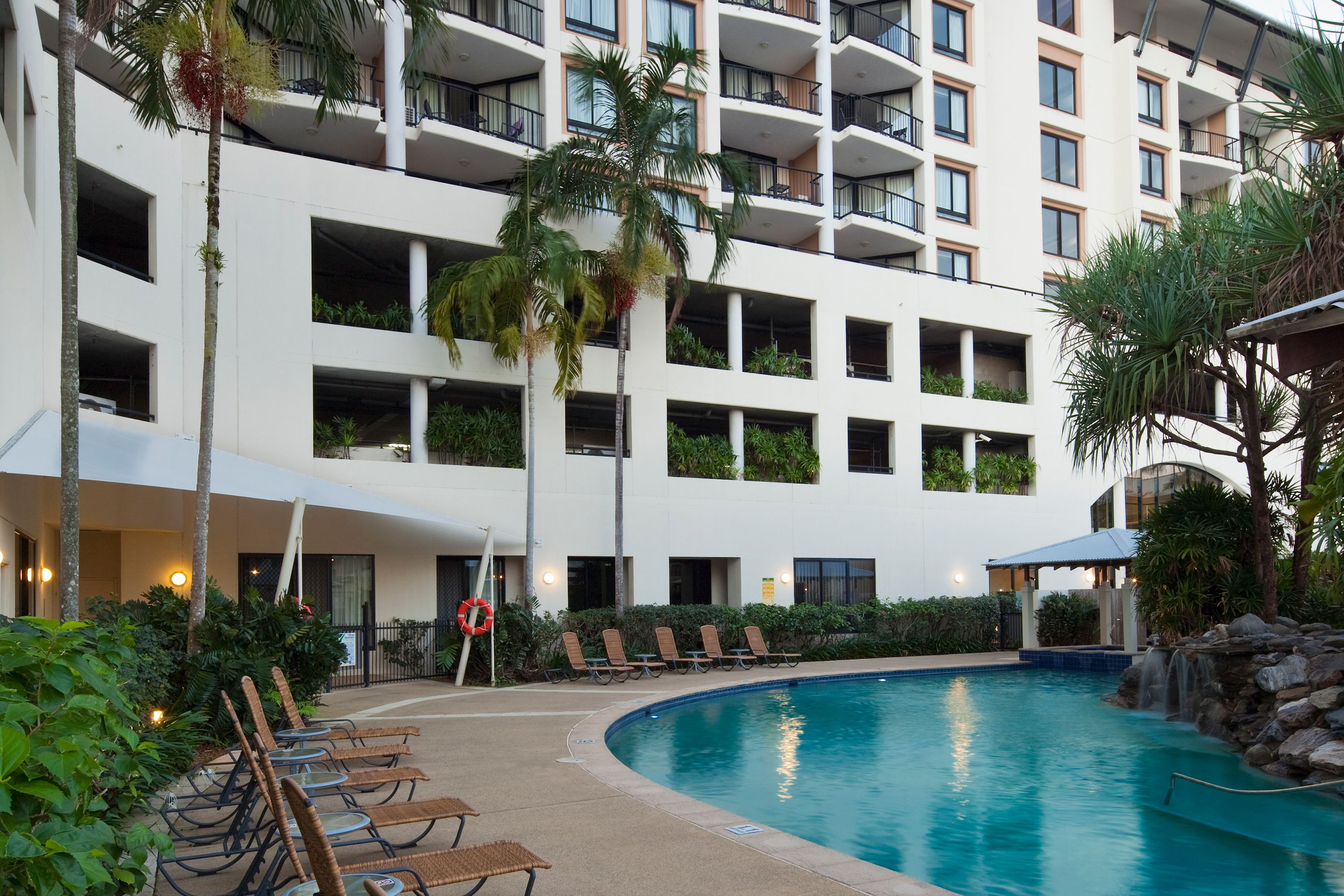 A hotel with a swimming pool, lounge chairs, and a palm tree.