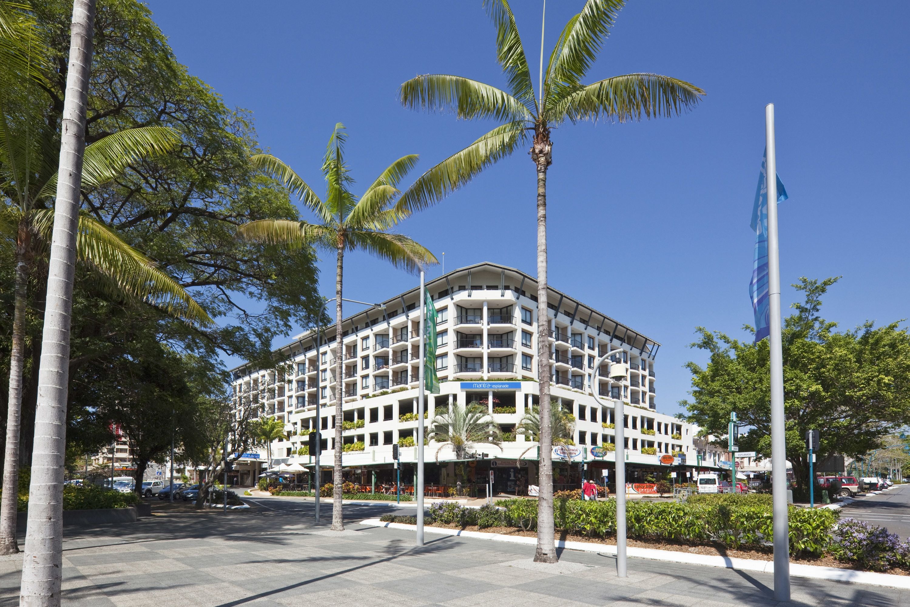 A multi-story hotel with balconies, surrounded by palm trees and a clear blue sky.