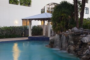 A swimming pool with a waterfall feature, surrounded by rocks and plants. - Mantra Esplanade (Cairns)