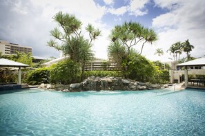 A swimming pool with a waterfall feature surrounded by tropical vegetation and palm trees. - Mantra Esplanade (Cairns)