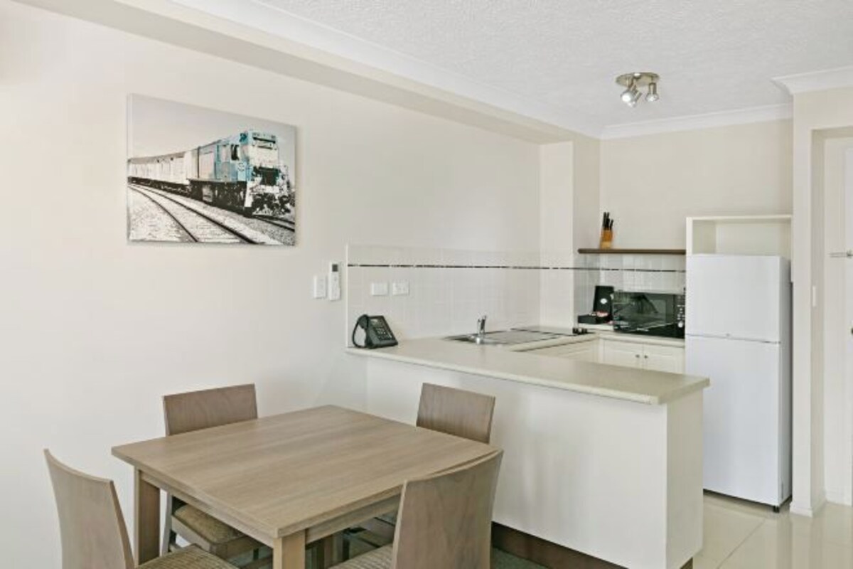 A compact kitchen with a dining area, a refrigerator, and a coffee maker.