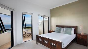 A bedroom with a large bed, a nightstand, a lamp, and a view of the sea through a sliding door.