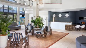 A spacious lobby with a reception desk, seating area with striped chairs, and large windows offering views of the outside. - Mantra Esplanade (Cairns)