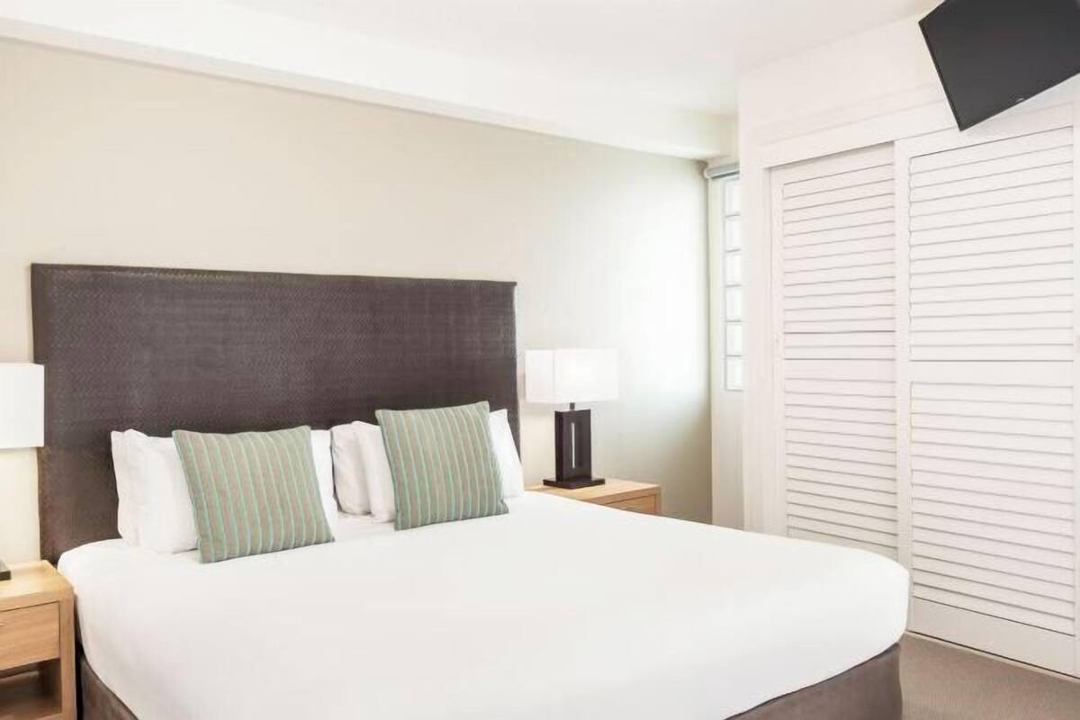Habitación de hotel con una cama grande, dos mesitas de noche con lámparas, un cabecero oscuro y un armario con puertas correderas.